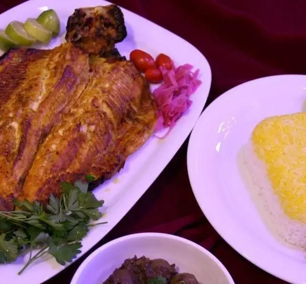 ماهی کبابی خوشمزه رستوران نازخاتون با برنج زعفرانی، لیمو، گوجه و ترشی. تجربه غذای اصیل ایرانی در نازخاتون.
