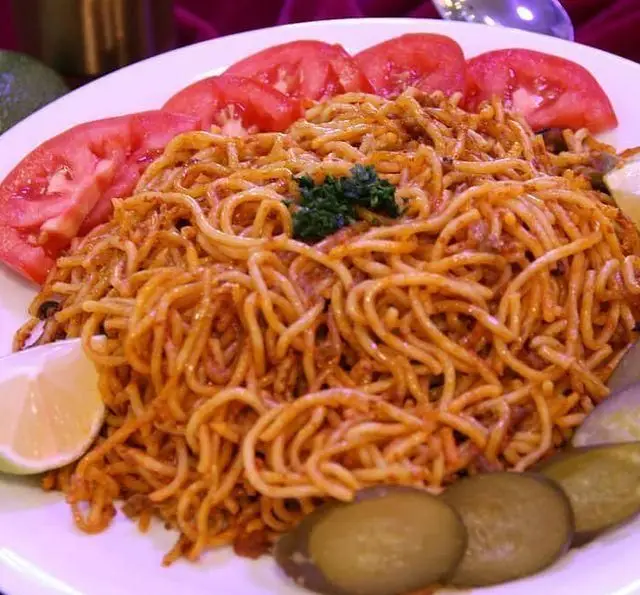 ماکارونی خوش طعم با سس قرمز و گوشت، همراه گوجه، خیارشور و لیمو در رستوران نازخاتون. غذایی خانگی و لذیذ.