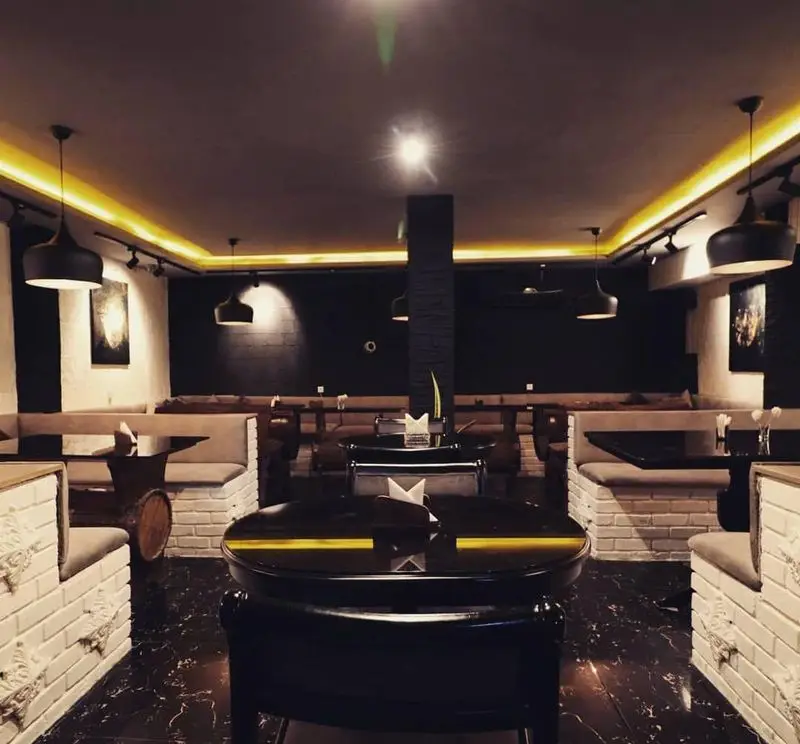 نمای داخلی کافه سنتی ژوان، با طراحی مدرن و سنتی، مبلمان راحتی با دیوارهای آجری سفید، میزهای مشکی و نورپردازی گرم، فضایی دنج و دلنشین.