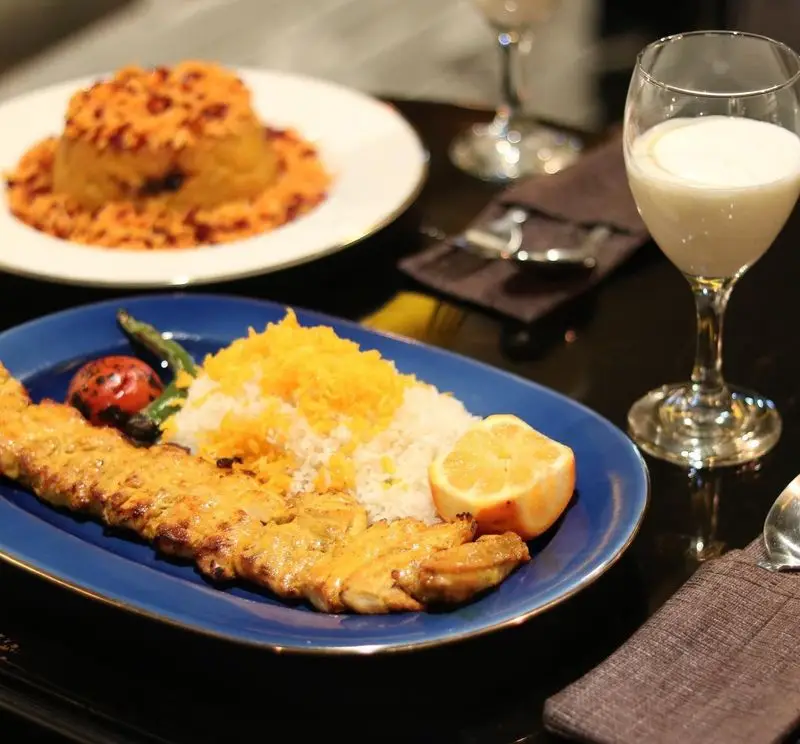 غذای اصیل ایرانی در کافه سنتی ژوان شامل جوجه کباب، برنج زعفرانی، گوجه کبابی و دوغ. تجربه‌ای لذت‌بخش از طعم‌های دلپذیر.