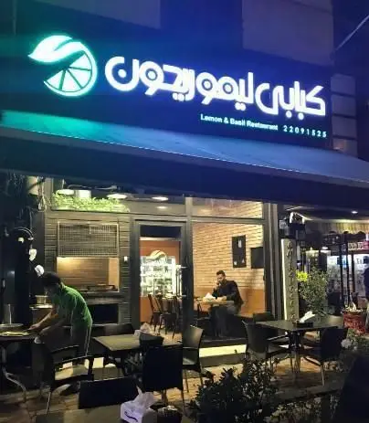 تصویری از نمای بیرونی رستوران کبابی لیمو ریحون در شب، با تابلو نورانی، میز و صندلی‌های فضای باز و داخل، آماده خدمات‌رسانی.