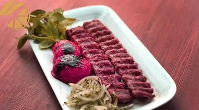 تصویری از سینی کباب کوبیده لذیذ کبابی لیمو ریحون، شامل کباب، گوجه کبابی، پیاز و سبزی تازه.