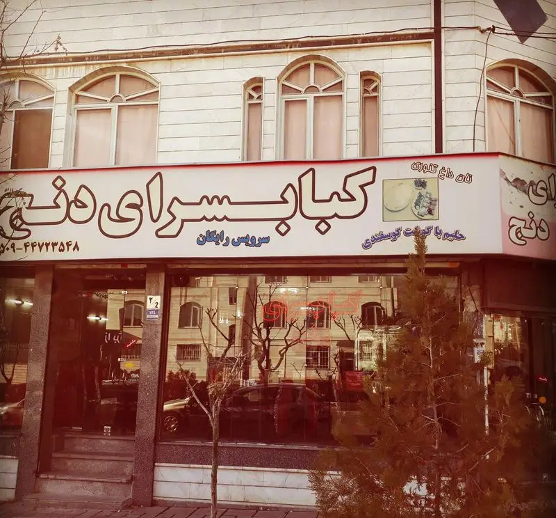 نمای خارجی رستوران کباب سرای دنج، با تابلوی حاوی شماره ۰۲۱-۴۴۷۷۲۲۵۸، سرویس رایگان، نان داغ تنوری و حلیم گوشت گوسفندی.