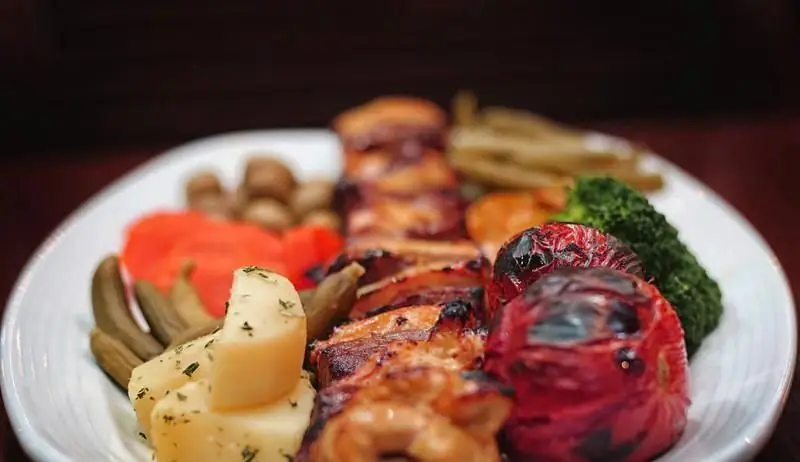 غذای لذیذ رستوران مدیا: بشقاب کباب گریل شده با گوشت آبدار و گوجه کبابی، به همراه بروکلی تازه، سیب زمینی، ترشی و دورچین کامل.