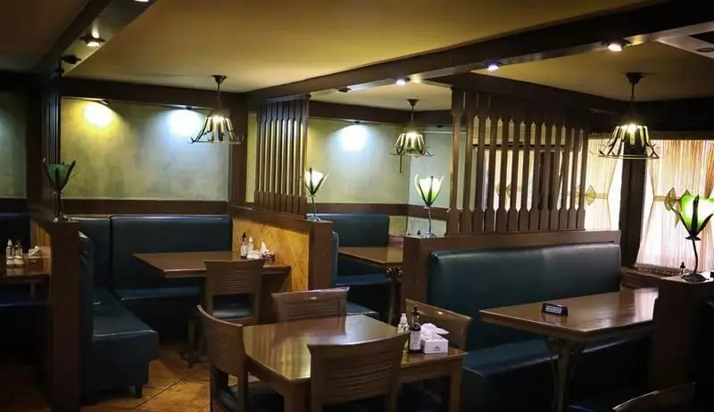 نمایی از فضای داخلی رستوران مدیا با دکوراسیون چوبی، میز و صندلی‌های شیک و مبلمان راحتی، ایده‌آل برای یک وعده غذای دنج.