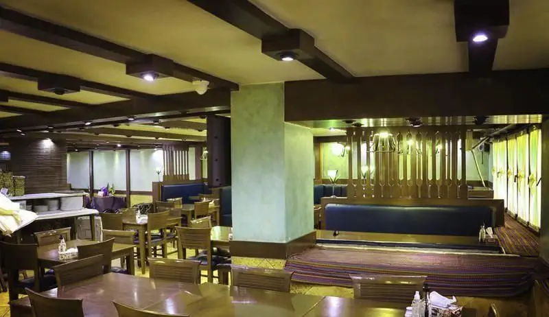 فضای داخلی رستوران مدیا با دکوراسیون چوبی، میز و صندلی‌های شیک، مبلمان آبی رنگ و نورپردازی دلنشین برای تجربه‌ای خاص.