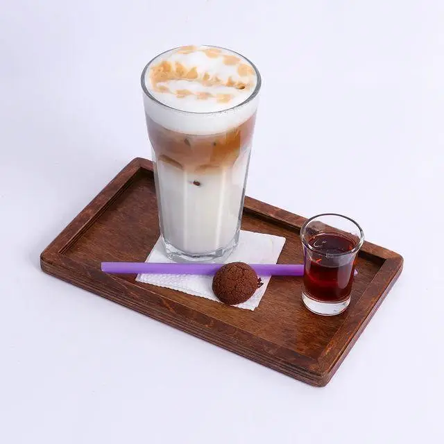 آیس لاته خوشمزه با فوم شیر و کارامل، همراه با شات و کوکی شکلاتی کوچک، سرو شده روی سینی چوبی در کافه لیدو پلاس
