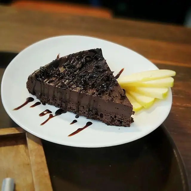 یک برش کیک شکلاتی غلیظ و خوشمزه، تزئین شده با شکلات رنده شده و سس، به همراه سیب‌های تازه اسلایس شده در کافه و کافی شاپ لیدو پلاس.
