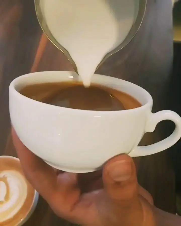 باریستای ماهر کافه و کافی شاپ لیدو پلاس در حال آماده‌سازی لاته با ریختن شیر فوم‌دار برای لاته آرت روی قهوه تازه.