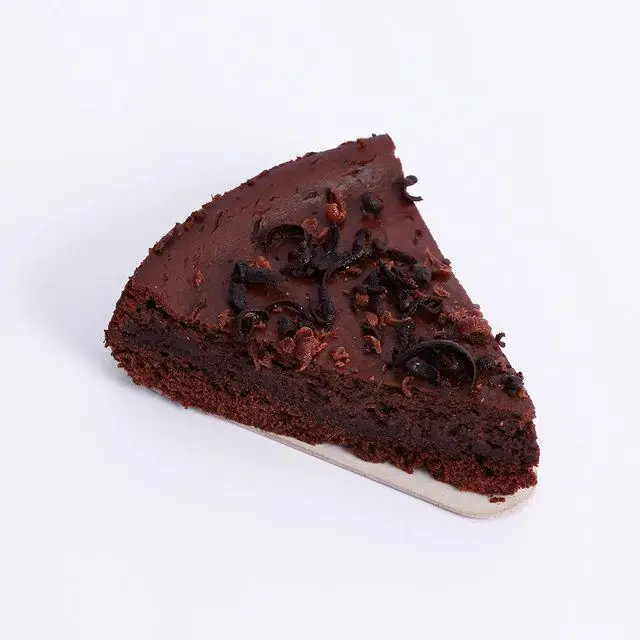 برش کیک شکلاتی خوشمزه و تازه کافه و کافی شاپ لیدو پلاس با روکش گاناش و تکه‌های شکلات، مناسب برای لذت بردن از طعم کاکائو.