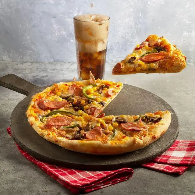 پیتزا با ذرت، سوسیس، فلفل و قارچ، با یک برش معلق و نوشیدنی گازدار در کافه و کافی شاپ لیدو پلاس، آماده سفارش.