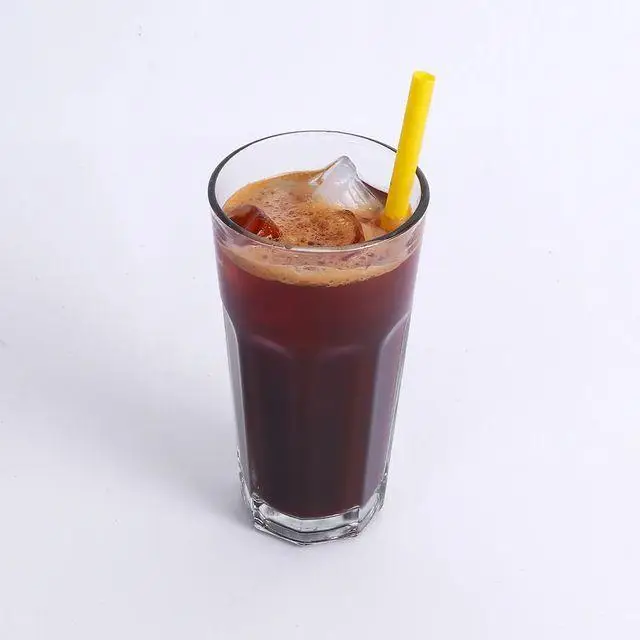 تصویری از یک لیوان قهوه سرد (آیس کافی یا کلد برو) با یخ و نی زرد در کافه و کافی شاپ لیدو پلاس. نوشیدنی خنک و دلچسب.