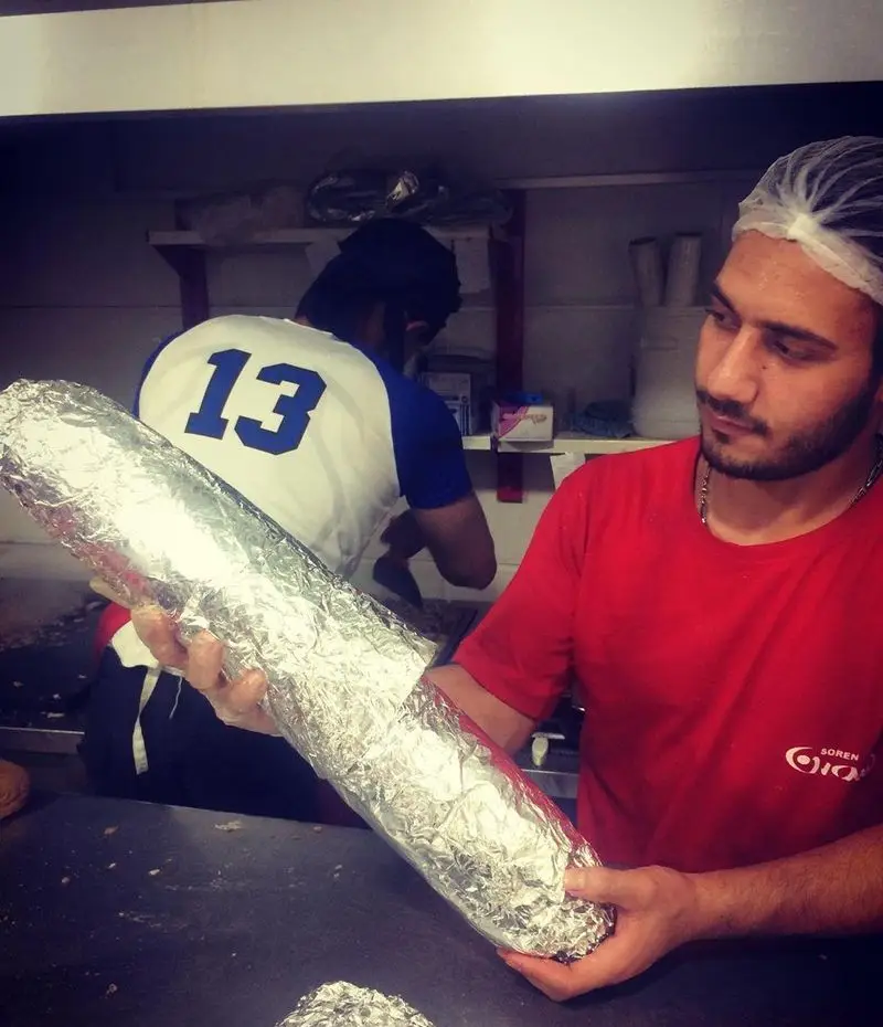 نمایی از ساندویچ فوق بزرگ زاپاتا در فست فود اژدر زاپاتا که توسط کارمند با دقت در فویل بسته‌بندی می‌شود.