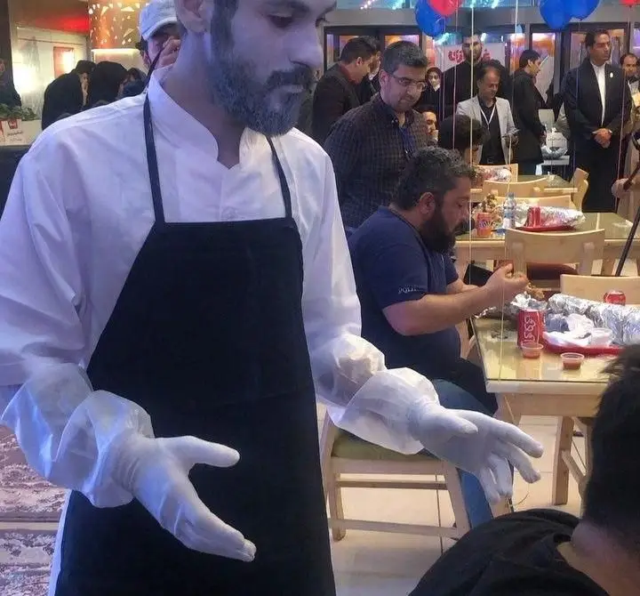 کارمند اژدر زاپاتا با پیشبند و دستکش در حال خدمت‌رسانی به مشتریان در محیط شلوغ و پر جنب و جوش فست فود اژدر زاپاتا.