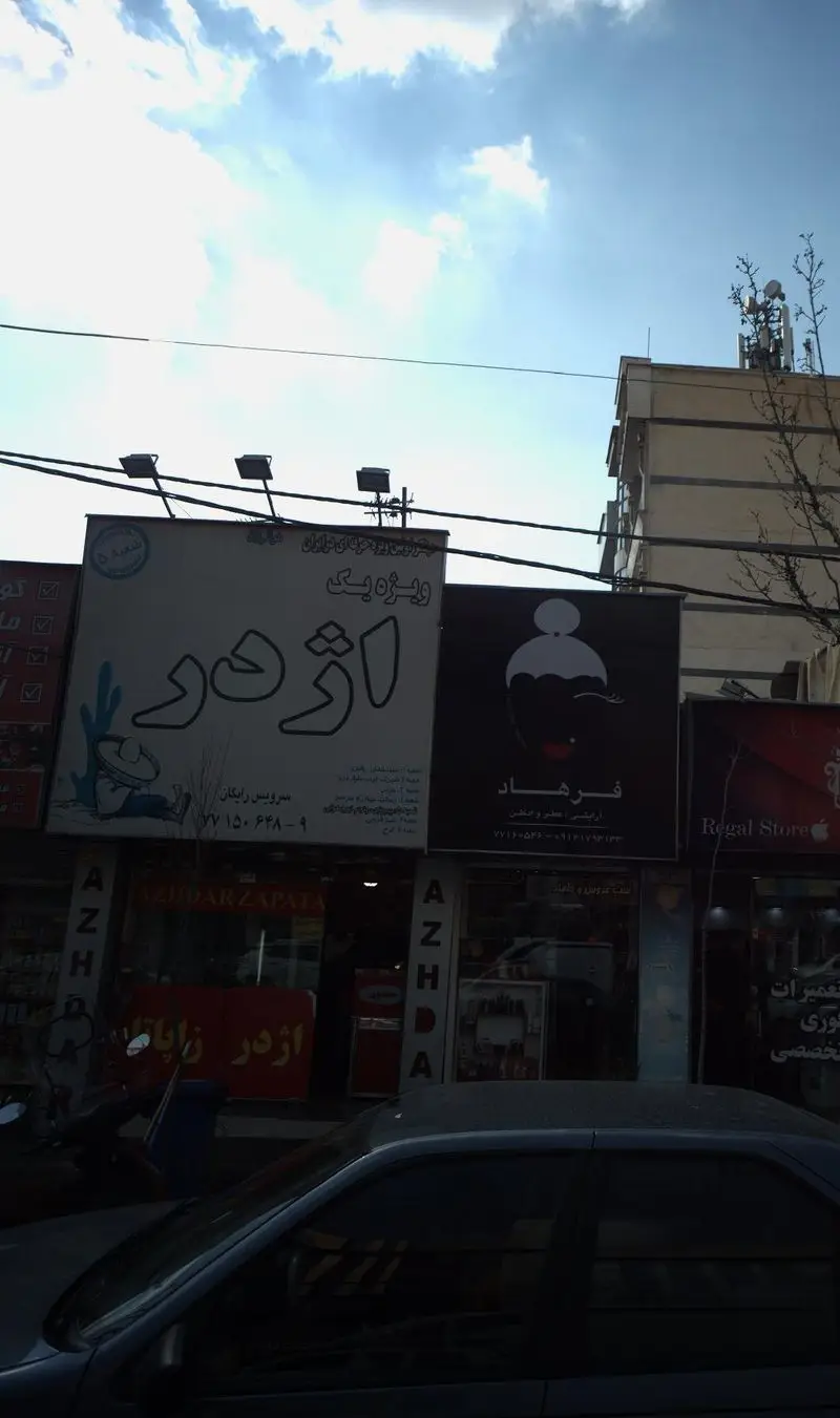 نمای کامل از فست فود اژدر زاپاتا، شامل تابلو اصلی با لوگوی ویژه یک و مرد مکزیکی، تابلوی فرهاد و آسمان آبی روشن با ابرهای پراکنده.