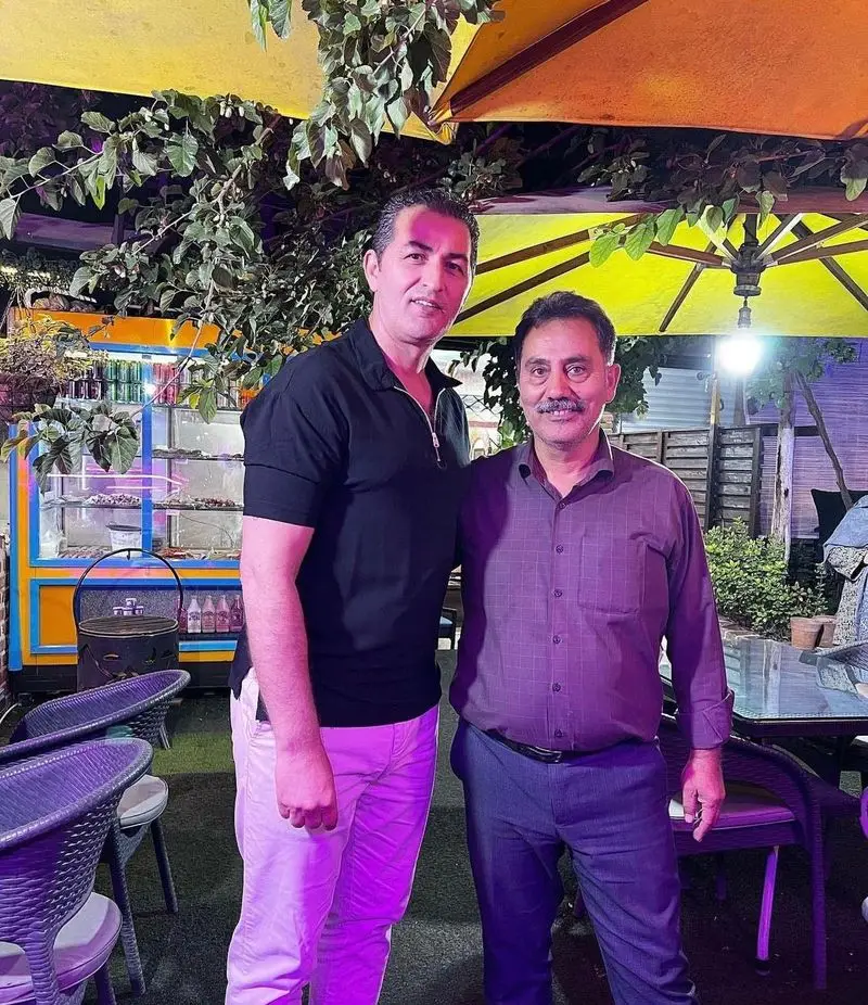 تصویری از دو نفر در فضای باز شبانه جگرسرای کلبه صحرا، مکانی عالی برای تجربه طعم لذیذ جگر و کباب در محیطی دلنشین و سرسبز.