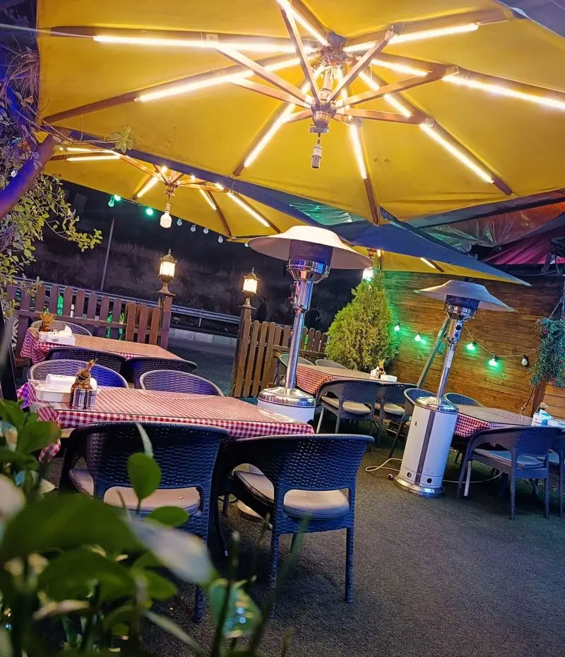 فضای باز و دلنشین جگرسرای کلبه صحرا در شب با چترهای نورانی زرد، میز و صندلی‌های شیک و گرمکن‌های مدرن برای مشتریان.