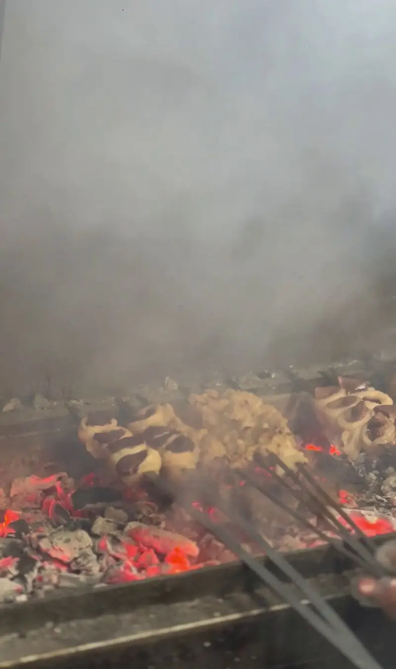 جگر کباب‌های تازه و لذیذ جگرسرای کلبه صحرا در حال پخت بر روی منقل ذغالی داغ، همراه با دود معطر و جذاب کباب.