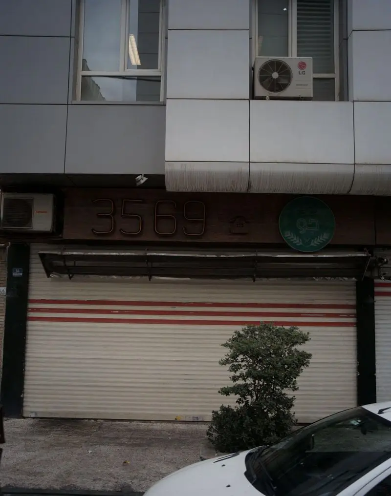 نمای بیرونی رستوران جو، با تابلوی نئونی شماره ۳۵۶۹، لوگوی سبز دایره‌ای، کرکره‌های فروشگاه و پنجره‌های ساختمان.