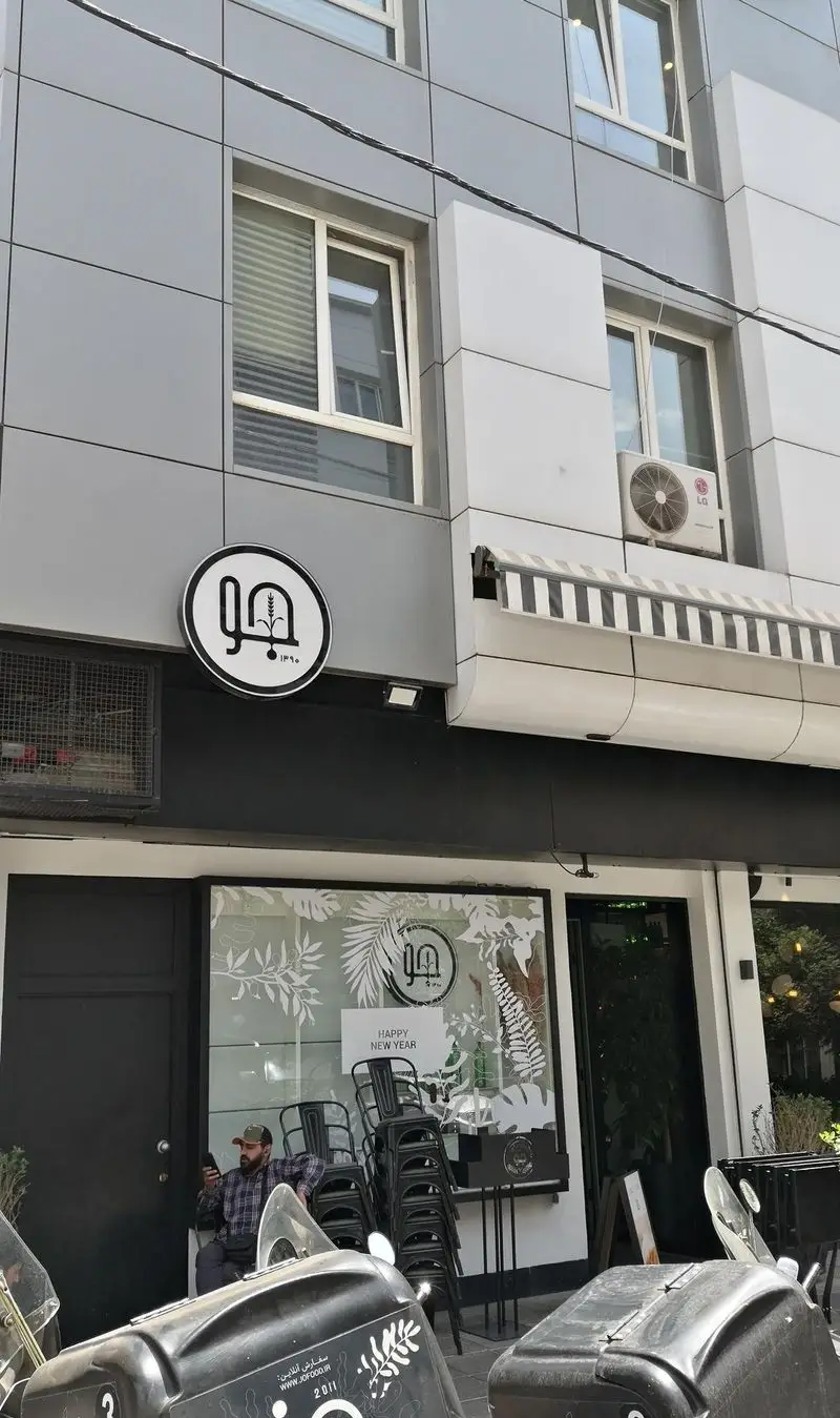 نمای بیرونی رستوران جو با تابلوی لوگوی دایره‌ای و مدرن، طراحی شیک ساختمان و پنجره‌های تزئین شده با شعار سال نو، فضایی دعوت‌کننده.