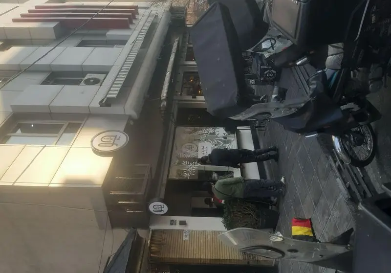 نمای بیرونی جذاب رستوران جو با مشتریان در ورودی، موتورسیکلت پارک شده، و تابلوی شیک آن، مکانی دنج برای لذت غذا.