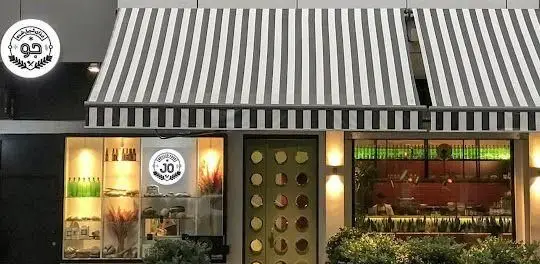 رستوران جو، نمای بیرونی شیک و مدرن با سایبان‌های سیاه و سفید، ورودی سبز رنگ و ویترین‌های روشن، تجربه دلنشین غذا.