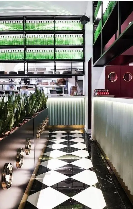 فضای داخلی شیک و مدرن رستوران جو، با طراحی دکوراسیون منحصربه‌فرد شامل کفپوش شطرنجی، قفسه‌های بطری سبز و گلدان‌های طبیعی.