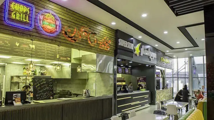 نمایی از کافی شاپ فوکورت آرتمیس با طراحی مدرن، پیشخوان‌های فعال چاپس گریل و سوپراستار، و مشتریانی که در فضای دلنشین مشغول صرف غذا هستند.