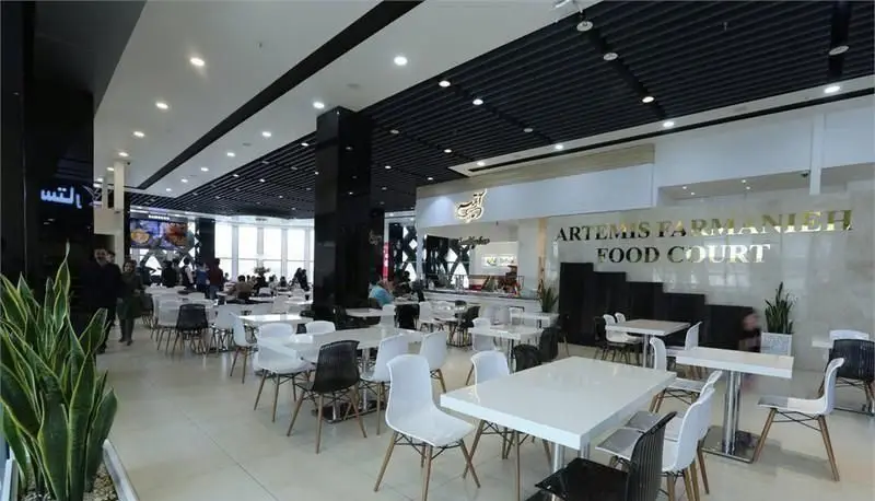 نمایی از فودکورت آرتمیس فرمانیه با میز و صندلی‌های مدرن، مشتریان و فضای دلنشین. کافی شاپ فوکورت آرتمیس.