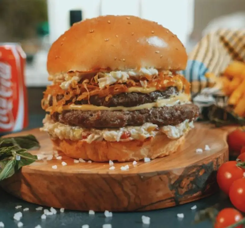 همبرگر دوبل لذیذ عطاویچ فردوس غرب با پنیر، پیاز سوخاری و سالاد کلم، کنار سیب زمینی سرخ کرده و نوشابه کوکا