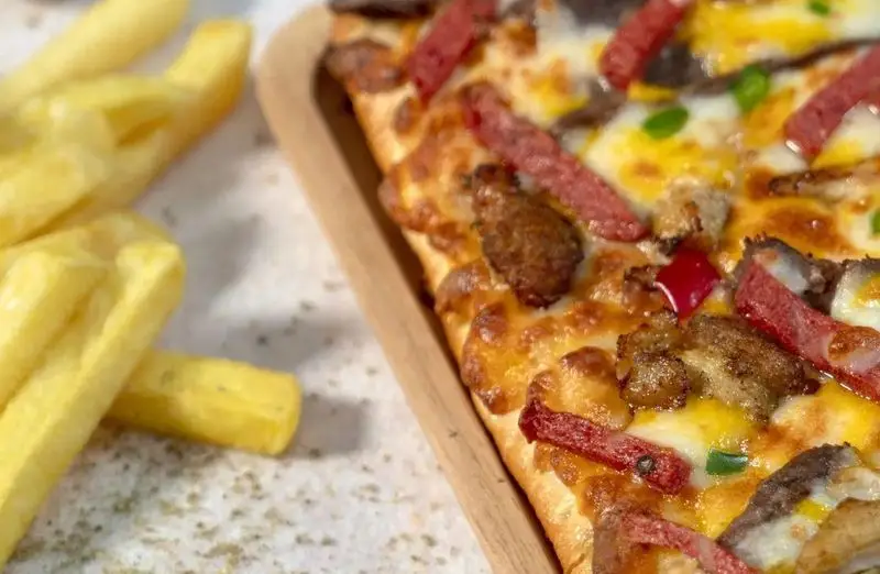 پیتزا مستطیلی و لذیذ عطاویچ فردوس غرب با تاپینگ‌های گوشت، پپرونی و قارچ، به همراه سیب‌زمینی سرخ‌کرده طلایی.