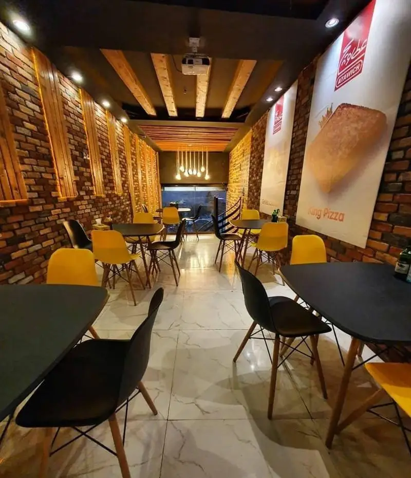 فضای داخلی مدرن عطاویچ فردوس غرب با دکوراسیون آجر و چوب، میز و صندلی‌های شیک و پوسترهای پیتزا. محیطی جذاب و دلنشین.