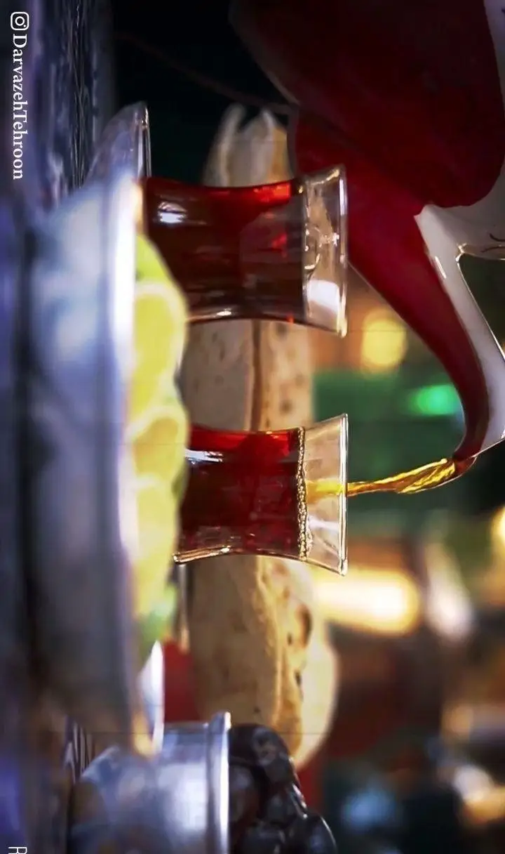 لحظه دلنشین سرو چای سنتی ایرانی از قوری به استکان‌ها، همراه با نان تازه و لیمو در محیط گرم رستوران رفتاری.