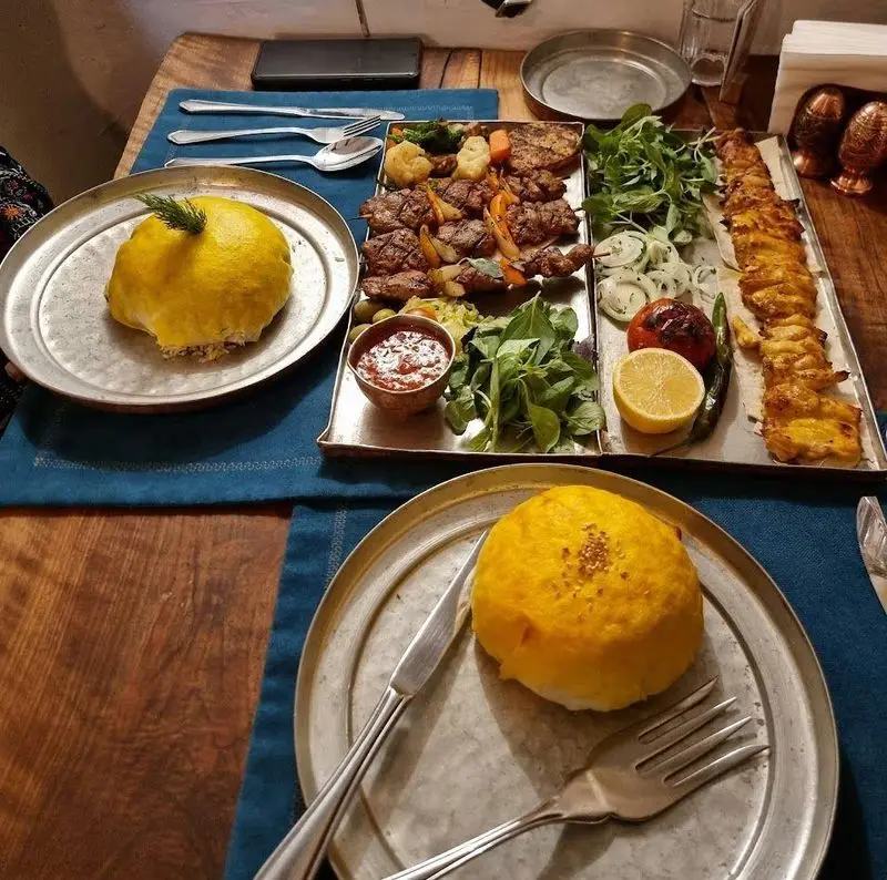 میز غذای مجلل در رستوران مس توران شامل انواع کباب‌های لذیذ، ته چین زعفرانی، سبزیجات تازه و مخلفات. طعم اصیل ایرانی را تجربه کنید.