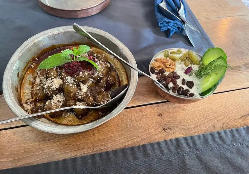 غذای اصیل و لذیذ رستوران مس توران شامل خورشت گوشت با تزئین نعنا و ماست و خیار با کشمش و گردو بر روی میز چوبی.