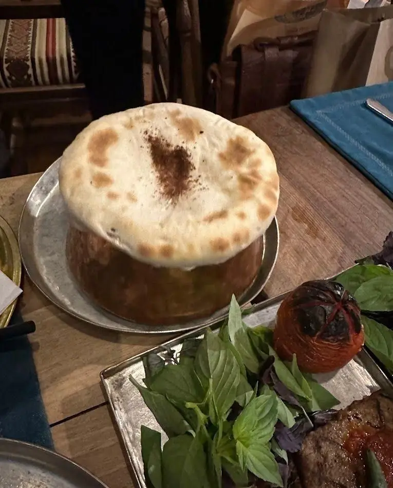 غذای سنتی و اصیل ایرانی در رستوران مس توران: یک دیزی با نان داغ روی آن، سرو شده روی سینی مسی با سبزی و گوجه کبابی.