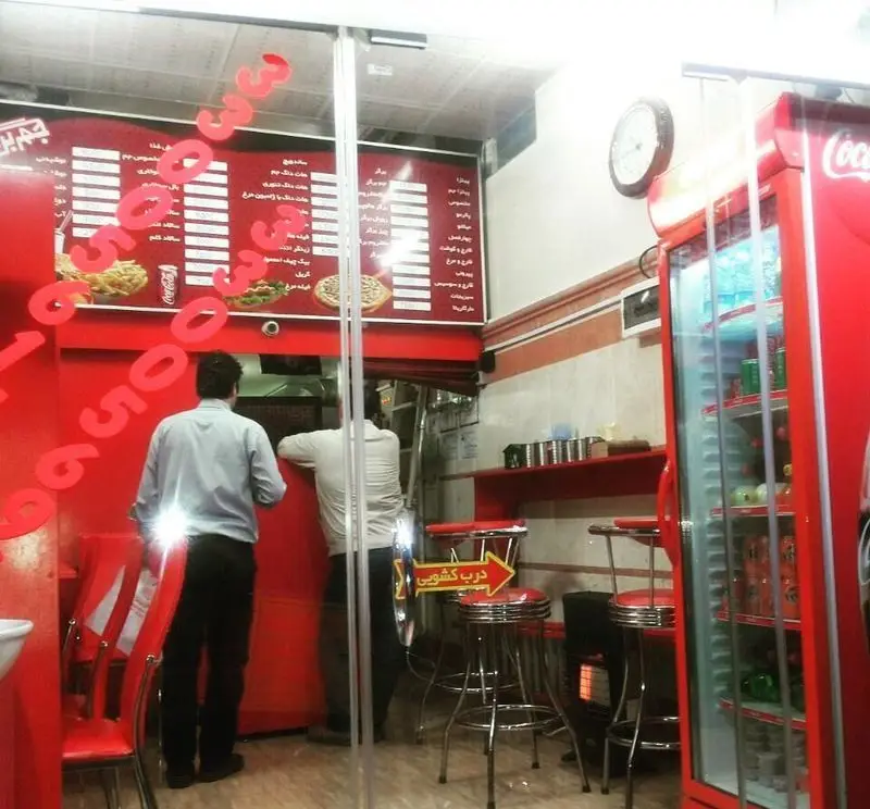 نمای داخلی فست فود جم برگر: منوی متنوع شامل برگر، پیتزا، ساندویچ و نوشابه، پرسنل در حال کار، یخچال و دکوراسیون مدرن قرمز و سفید.