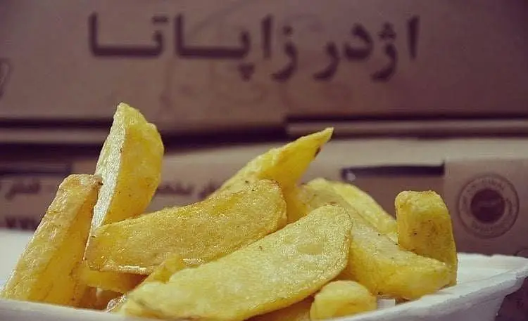 سیب زمینی سرخ کرده درشت و طلایی در یک ظرف سفید، با پس زمینه تار جعبه فست فود اژدر زاپاتا که نام رستوران روی آن است.