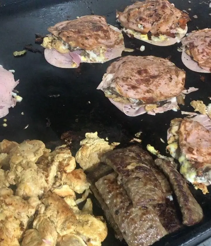 ساندویچ‌های ویژه فست فود اژدر زاپاتا شامل ژامبون، تخم مرغ و انواع گوشت گریل شده در حال پخت روی سینی داغ.