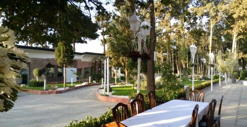 نمایی زیبا از فضای باز رستوران فرسکا با میز و صندلی‌های چوبی در میان درختان سرسبز و دکوراسیون شیک برای مهمانی‌ها و دورهمی‌ها