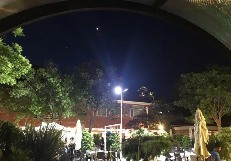 نمای شب فضای باز و دلنشین رستوران فرسکا، با چیدمان زیبا از میز و صندلی‌ها در زیر نور ماه و درختان سرسبز، محیطی ایده‌آل برای شام.