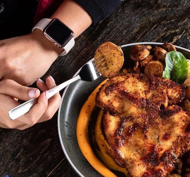 یک وعده غذای دلپذیر در کافه رستوران مونلانژ: مرغ گریل، سیب‌زمینی برشته، قارچ و سس ویژه، با ساعت هوشمند روی مچ دست.