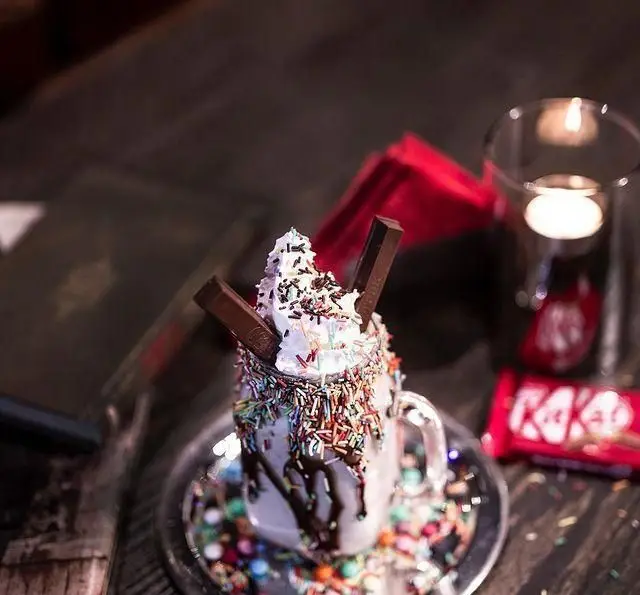 مانستر شیک شکلاتی کافه رستوران مونلانژ با خامه فراوان، اسپرینکلز رنگارنگ و تزیین کیت کت. بهترین دسر و نوشیدنی خنک.