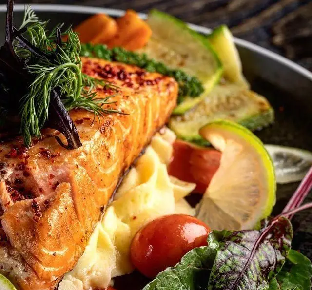 سالمون گریل شده آبدار با پوره سیب‌زمینی، گوجه گیلاسی و سبزیجات تازه. غذایی اشتهاآور و سالم از کافه رستوران مونلانژ.