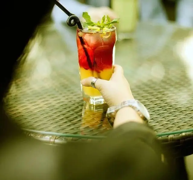 نوشیدنی کوکتل خنک و جذاب با لایه‌های رنگارنگ و نعناع تازه در دست مشتری در کافه رستوران مونلانژ، تجربه‌ای دلپذیر از طعم‌ها.