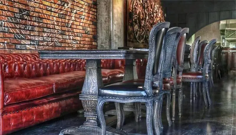 فضای داخلی جذاب کافه رستوران مونلانژ: مبلمان چرمی قرمز، میز و صندلی‌های چوبی تیره حکاکی شده و دیوار آجری با نقوش هنری، دکوری لوکس و آرامش‌بخش.