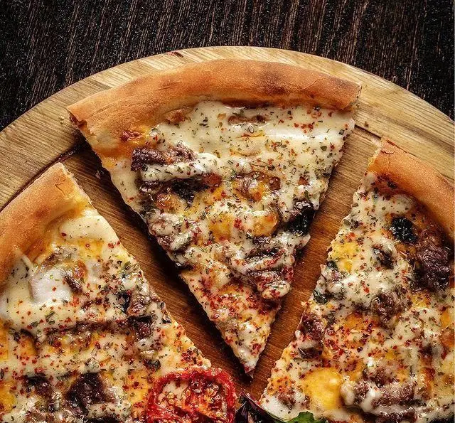 پیتزای خوشمزه کافه رستوران مونلانژ با پنیر، گوشت، ادویه و سبزیجات معطر روی تخته سرو چوبی. تجربه‌ای لذیذ از غذای ایتالیایی.