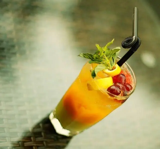 کوکتل میوه‌ای رنگارنگ و خنک کافه رستوران مونلانژ، با لایه‌های جذاب و تزئین شده با نعناع، لیمو و انگور قرمز برای روزهای گرم.