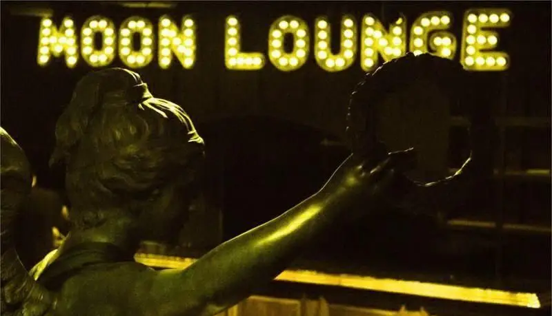 نمایی جذاب از تابلوی نورانی MOON LOUNGE و مجسمه در ورودی کافه رستوران مونلانژ با دکوراسیونی خاص در شب.