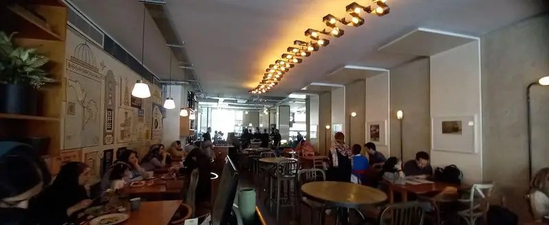 فضای داخلی پرجنب‌وجوش کافه روبرتو با مشتریانی که در حال لذت بردن از نوشیدنی و غذا هستند. دکوراسیون خاص با نورپردازی گرم و طراحی دیواری مدرن.